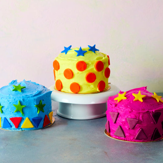 Three mini cakes in primar colors, with fondant cut out decorations.