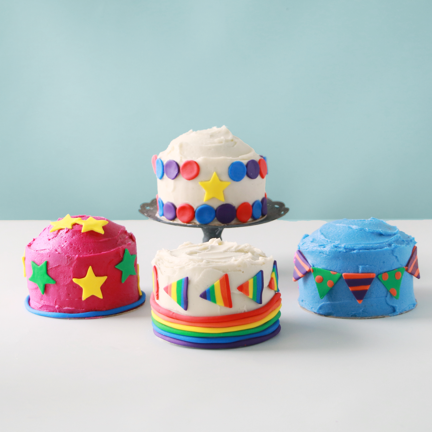 Four mini cakes, decorated with colored buttercream and fondant